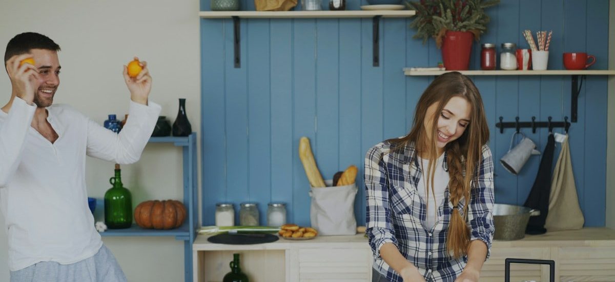 Attractive loving couple having fun in the kitchen. Handsome man juggle with fruits to impress his girlfriend at home