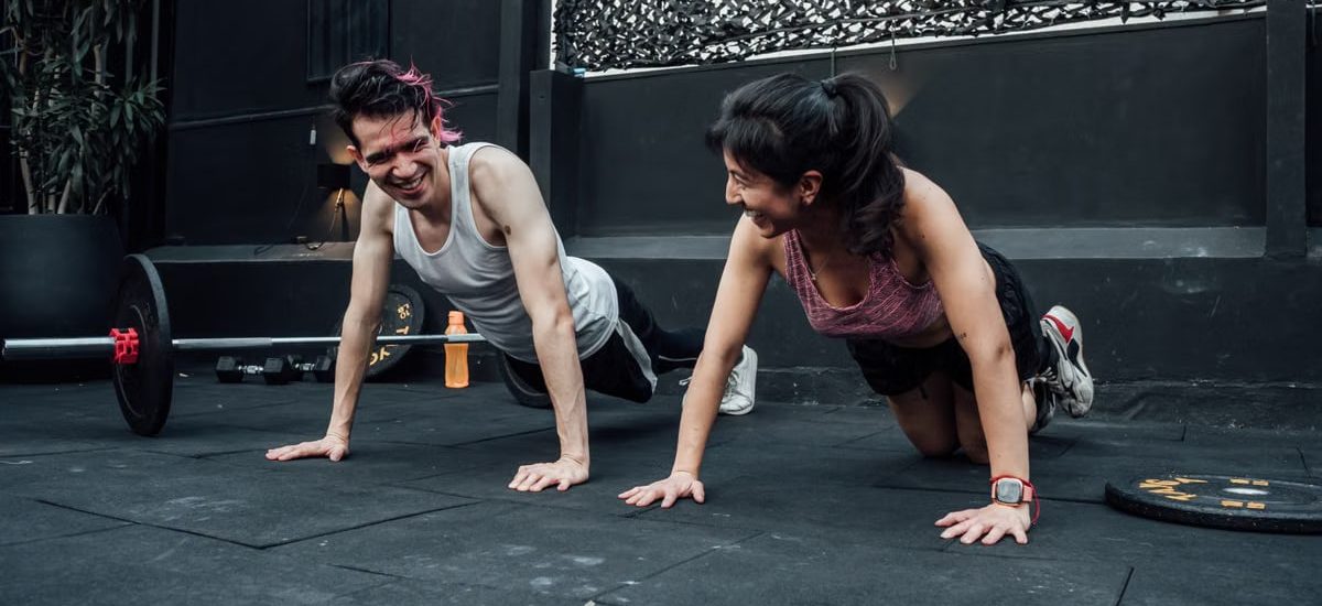 Man and woman doing pushups while smiling during a workout inside a Mexico City gym.